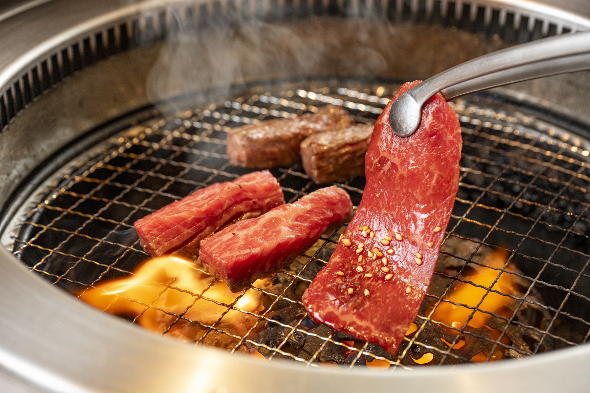 炭火の上で香ばしく焼き上がる焼肉と立ちのぼる湯気が伝わる店内の食事風景